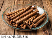 Ceylon cinnamon sticks in glass plate on wooden board, rustic style. Still life natural food of sri lankan cinnamon sticks on table at grey wall. Delicious tasty healthy concept. Copy ad text space. Стоковое AI-изображение, AI-художник Aleksandr Golubev / Фотобанк Лори