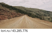 A bumpy dirt road winds through a forested landscape, framed by majestic mountains in the distance. Стоковое видео, видеограф ILIA GOROKHOV / Фотобанк Лори