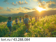 A group of children with backpacks runs through a green meadow against the backdrop of sunset. The sun shines brightly, painting the sky and clouds in warm colors. Children run through the grass, surrounded by wild flowers and green hills, creating an atmosphere of freedom and joy. Mountains can be seen in the distance, emphasizing the beauty of nature and the breadth of the landscape. Стоковое AI-изображение, AI-художник Анна Кривицкая / Фотобанк Лори