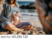 Relaxation, peace of mind, sea air. Close-up of the tummy. A pregnant woman on the beach by the sea. The concept of pregnancy, childbirth and parental responsibilities. Стоковое AI-изображение, AI-художник Photojuli / Фотобанк Лори