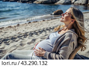 Relaxation, peace of mind, sea air. Close-up of the tummy. A pregnant woman on the beach by the sea. The concept of pregnancy, childbirth and parental responsibilities. Стоковое AI-изображение, AI-художник Photojuli / Фотобанк Лори