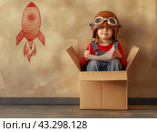 Child in Cardboard Box with Aviator Helmet and Rocket Drawing. Стоковое AI-изображение, AI-художник Кирилл Черезов / Фотобанк Лори