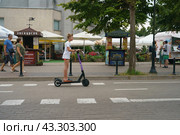 Svetlogorsk, Kaliningrad oblast, Russia -  August 20, 2022: Teenager drives motor scooter on the city street in summer day  Side view. He squeezed his eyes shut and rushes along the roadway. Редакционное фото, фотограф YuryKara / Фотобанк Лори