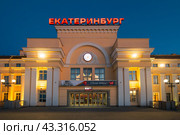 Здание вокзала железнодорожной станции Екатеринбург-Пассажирский, город Екатеринбург, Свердловская область, Россия. Свердловская железная дорога. Вечерний вид на здание вокзала со стороны платформы. На крыше вывеска «Екатеринбург». Над входом баннер с текстом «9 мая, С Днём Победы!» и логотипом РЖД. На фасаде часы. (2023 год). Редакционное фото, фотограф Андрей Степанов / Фотобанк Лори