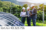A group of engineers stands with drawings near a solar panel on a green lawn. Ecology of energy. Стоковое AI-изображение, AI-художник Ярославский Максим / Фотобанк Лори