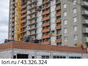 Рабочий забирается в строительную люльку для выполнения работ на фасаде здания на высоте. Фасад здания оштукатурен цементной смесью. Рабочий-высотник в каске. Стоковое фото, фотограф Эдуард Белкин / Фотобанк Лори