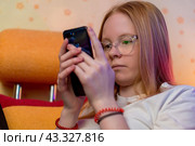 Милая девушка-подросток в очках сидит и смотрит на дисплей смартфона. Стоковое фото, фотограф Валуйских Владимир / Фотобанк Лори