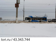 Движение троллейбуса с автономным ходом с опущенными токосъёмниками по заснеженной улице, Волгоград, улица Николая Отрады , Россия (2024 год). Редакционное фото, фотограф Андрей Цыганков / Фотобанк Лори