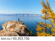 Baikal Lake in autumn. A happy tourist rejoices at his arrival at the lake and raises his hands to meet the Small Sea while standing on a rock on the shore of Olkhon Island on a sunny clear October day. Стоковое фото, фотограф Виктория Катьянова / Фотобанк Лори