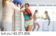 Focused teenage girl wearing boxing gloves working out with female coach during self-defense course, practicing punches on mitts. Стоковое видео, видеограф Яков Филимонов / Фотобанк Лори