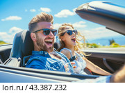 A man and a woman are chuckling as they drive a convertible car under the sky with sunglasses on. Стоковое AI-изображение, AI-художник Юрий Поздников / Фотобанк Лори