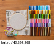 Accessories for hand embroidery with satin ribbons: canvas in hoop, pincushion with needles, set of multi-colored satin ribbons, scissors, hook and needle threader on wooden table. Flat lay, closeup, mockup. Стоковое фото, фотограф Виктория Катьянова / Фотобанк Лори