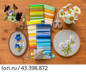 Two summer floral hand embroideries with satin ribbons of pansies and daisies in hoops, bouquets of flowers on wooden table. Nearby is set of satin ribbons, needles and scissors for work. Flat lay, close-up. Стоковое фото, фотограф Виктория Катьянова / Фотобанк Лори