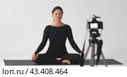 A woman video blogger, yoga instructor communicates with her audience sitting in a relaxed butterfly pose, practices meditation, records a video tutorial. Стоковое видео, видеограф Сергей Чайко / Фотобанк Лори