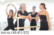 Group of women of various ages, passionate about ballet, friendly chatting while relaxing at barre after intense rehearsal in well-lit dance studio. Стоковое видео, видеограф Яков Филимонов / Фотобанк Лори