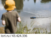 A 5-year-old boy in a yellow panama hat launches a radio-controlled boat in a pond. Children's fun and street games. Child's leisure time. Стоковое фото, фотограф Photojuli / Фотобанк Лори