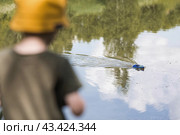 A 5-year-old boy in a yellow panama hat launches a radio-controlled boat in a pond. Children's fun and street games. Child's leisure time. Стоковое фото, фотограф Photojuli / Фотобанк Лори
