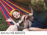 Summer holidays for children in the fresh air. A cute little boy with his father is having fun on a hammock in the backyard. A child and a dad in a hammock. Стоковое фото, фотограф Photojuli / Фотобанк Лори