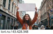 A young woman on a city street shows a large empty sign above her head. Street protests and demonstrations concept, banner with copy space. Стоковое AI-изображение, AI-художник Александр Довянский / Фотобанк Лори