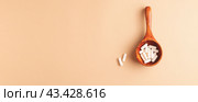 Top view of wooden spoon with white capsules on beige background. Стоковое фото, фотограф Юлия Трикашная / Фотобанк Лори