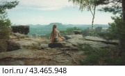 A woman sits meditating on a rocky ledge with a panoramic view of the Bastei Elbe Sandstone Mountains in Germany. Стоковое видео, видеограф Igor Tichonow / Фотобанк Лори
