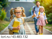 A cute girl with glasses shows the class with her hand. The child goes to school for the first time. A child with a school bag and a book. A child in the classroom on the background of a blackboard. Back to school. Стоковое AI-изображение, AI-художник Photojuli / Фотобанк Лори