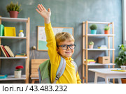 A boy with glasses shows the class with his hand. The child goes to school for the first time. A child with a school bag and a book. A child in the classroom on the background of a blackboard. Back to school. Стоковое AI-изображение, AI-художник Photojuli / Фотобанк Лори