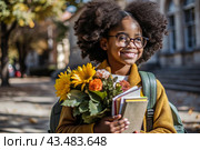 A pretty black African American woman in glasses with a bouquet of autumn flowers goes to school for the first time. A child with a school bag, a book and flowers. A child on a city street. Back to school. Стоковое AI-изображение, AI-художник Photojuli / Фотобанк Лори