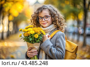 A cute little curly-haired girl with glasses and a bouquet of autumn flowers goes to school for the first time. A child with a school bag, a book and flowers. A child on a city street. Back to school. Стоковое AI-изображение, AI-художник Photojuli / Фотобанк Лори
