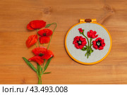 Flat lay of floral hand embroidery with satin ribbons of red poppy flowers in hoops on wooden background. Crafts and embroidery as hobby and leisure. Top view, close-up, mock up, copy space. Стоковое фото, фотограф Виктория Катьянова / Фотобанк Лори