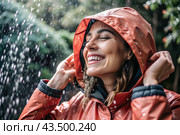 Close-up. A happy young woman in a raincoat enjoys the rain on the background of a green forest, the concept of enjoying a natural leisurely life, environment, lifestyle. Стоковое AI-изображение, AI-художник Photojuli / Фотобанк Лори