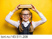 A pretty girl with glasses and books on her head. The child goes to school for the first time. A child on a yellow monochrome background. Back to school. Стоковое AI-изображение, AI-художник Photojuli / Фотобанк Лори