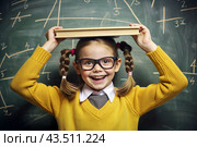 A pretty girl with glasses and books on her head. The child goes to school for the first time. A child in the classroom on the background of a blackboard. Back to school. Стоковое AI-изображение, AI-художник Photojuli / Фотобанк Лори