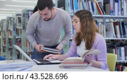 Emotional student girl, preparing for classes on a laptop with a guy classmate in the university library, points him to something in the monitor. Стоковое видео, видеограф Яков Филимонов / Фотобанк Лори