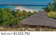 Postcard tropical landscape. A sandbar winds through the aquamarine ocean towards the green island. The boat is at the shore. People on the beach. In the foreground the thatched roof of the bungalow. Стоковое фото, фотограф Вера Ивановна Кубарева / Фотобанк Лори