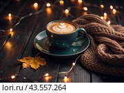 A seasonal drink. Delicious hot cappuccino in a mug with a saucer and a knitted snood, a scarf on a wooden table in the interior of the cafe. It's a rainy autumn day. Стоковое AI-изображение, AI-художник Photojuli / Фотобанк Лори