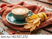 A seasonal drink. Delicious hot cappuccino in a mug with a saucer and a knitted snood, a scarf on a wooden table in the interior of the cafe. It's a rainy autumn day. Стоковое AI-изображение, AI-художник Photojuli / Фотобанк Лори