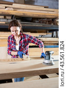 During manufacturing, woman employee grinds surface of wooden board, gives smoothness to surface. Стоковое фото, фотограф Яков Филимонов / Фотобанк Лори