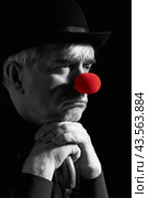 Dramatic selective color portrait of a clown against a dark background leaning on the handle of an umbrella. Стоковое фото, фотограф Сергей Пристяжнюк (Serg Zastavkin) / Фотобанк Лори