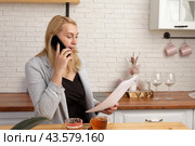 Businesswoman talking on the phone while reading a document in the kitchen. Стоковое фото, фотограф Светлана Акифьева / Фотобанк Лори