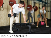 Athletic guy doing crossfit with dumbbells in the gym, leaning on bench. Стоковое фото, фотограф Яков Филимонов / Фотобанк Лори
