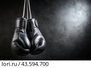 Professional black boxing gloves hang on a black background with a space to copy. Стоковое AI-изображение, AI-художник Photojuli / Фотобанк Лори