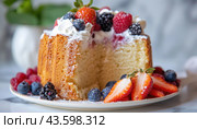 A Bundt cake is displayed on a plate with whipped cream and berries, one slice already eaten. Стоковое AI-изображение, AI-художник Юрий Поздников / Фотобанк Лори