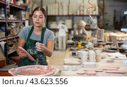 Young female worker in pottery factory lowers fired clay plates and cups into container with glaze. Стоковое фото, фотограф Яков Филимонов / Фотобанк Лори