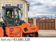 Небольшой каток уплотняет новую асфальтированную дорогу в коттеджном поселке в горной местности (2024 год). Редакционное фото, фотограф Сергей Сергеев / Фотобанк Лори