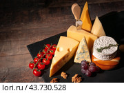 Various types of cheese on rustic wooden table. Different types of cheeses. slices of cheese brie or camembert with parmesan, cheddar, gouda, roquefort with nuts on dark board on wooden background. Стоковое фото, фотограф Павел Муравьев / Фотобанк Лори
