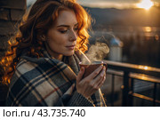A red-haired, beautiful woman wrapped in a plaid with a mug of hot coffee on a beautiful patio in the rays of the setting sun. The girl inhales the aroma of the drink. Comfort and harmony. Стоковое AI-изображение, AI-художник Photojuli / Фотобанк Лори