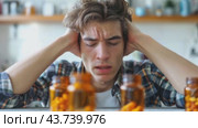 Young man holding his head in pain surrounded by pill bottles. Стоковое AI-видео, аниматор Юрий Поздников / Фотобанк Лори