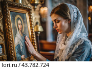 Portrait of a beautiful young woman in a headscarf in an Orthodox church. A girl prays in a church against the background of icons. Стоковое AI-изображение, AI-художник Photojuli / Фотобанк Лори