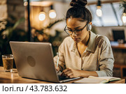 A young female freelance businessman in glasses and headphones is working on a laptop or shopping in an online store. The woman is writing something in a notebook. Стоковое AI-изображение, AI-художник Photojuli / Фотобанк Лори